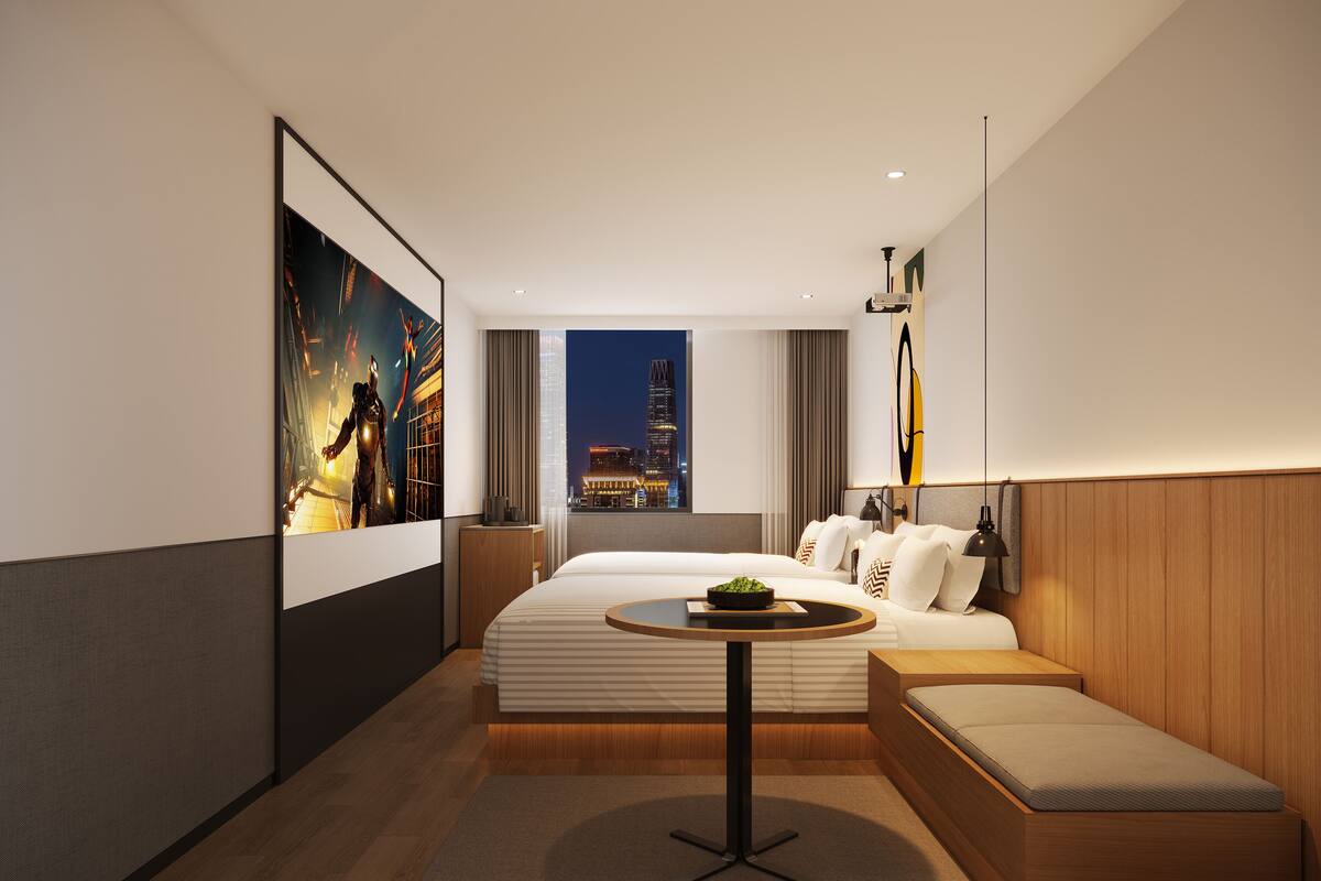 A modern hotel room with a large bed, a small round table, and a city view.