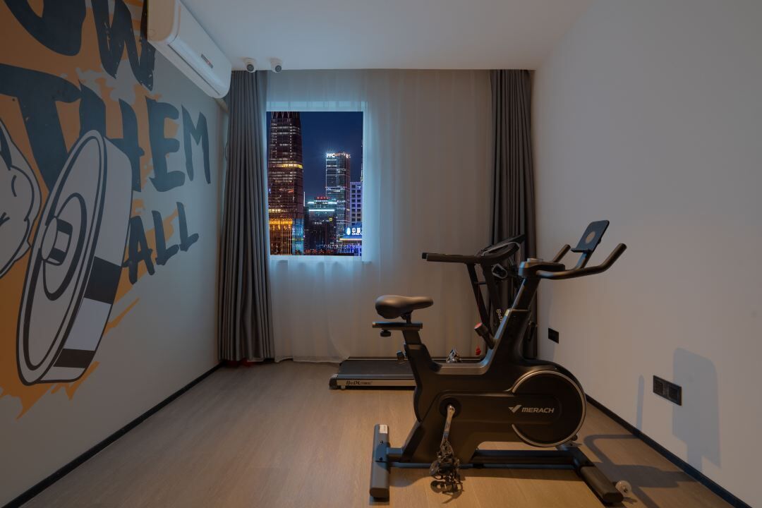 A hotel room with a cityscape view through a window, a treadmill, and a wall mural.