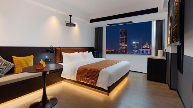 A modern hotel room with a large bed, a seating area with a table, and a view of a cityscape at night. - Mcsrh Hotel -Hangzhou West Lake (Hangzhou)
