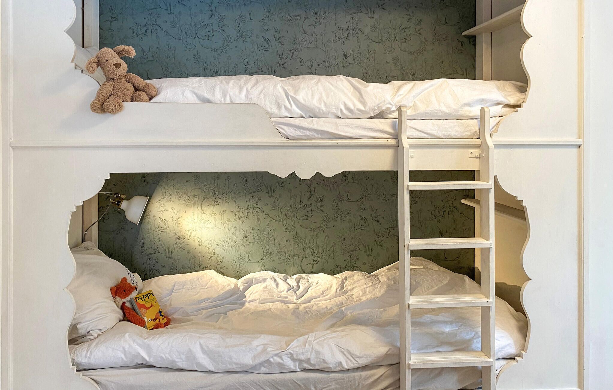 Un lit superposé avec une échelle, un ours en peluche et un livre sur le lit du bas.