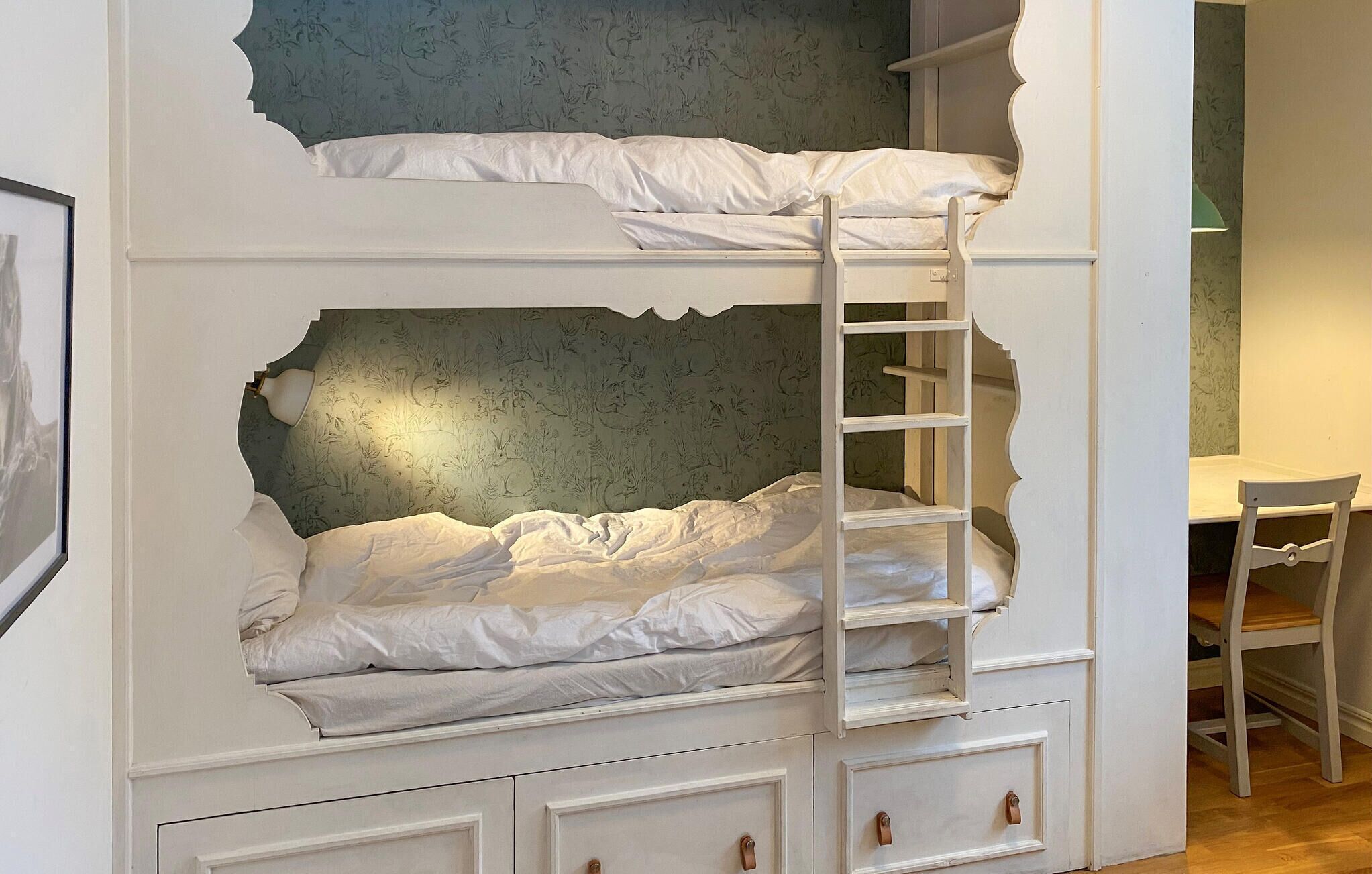 Ein Stockbett mit einer Leiter, einem Schreibtisch und einem Stuhl in einem Zimmer mit gemustertem Wandpapier.