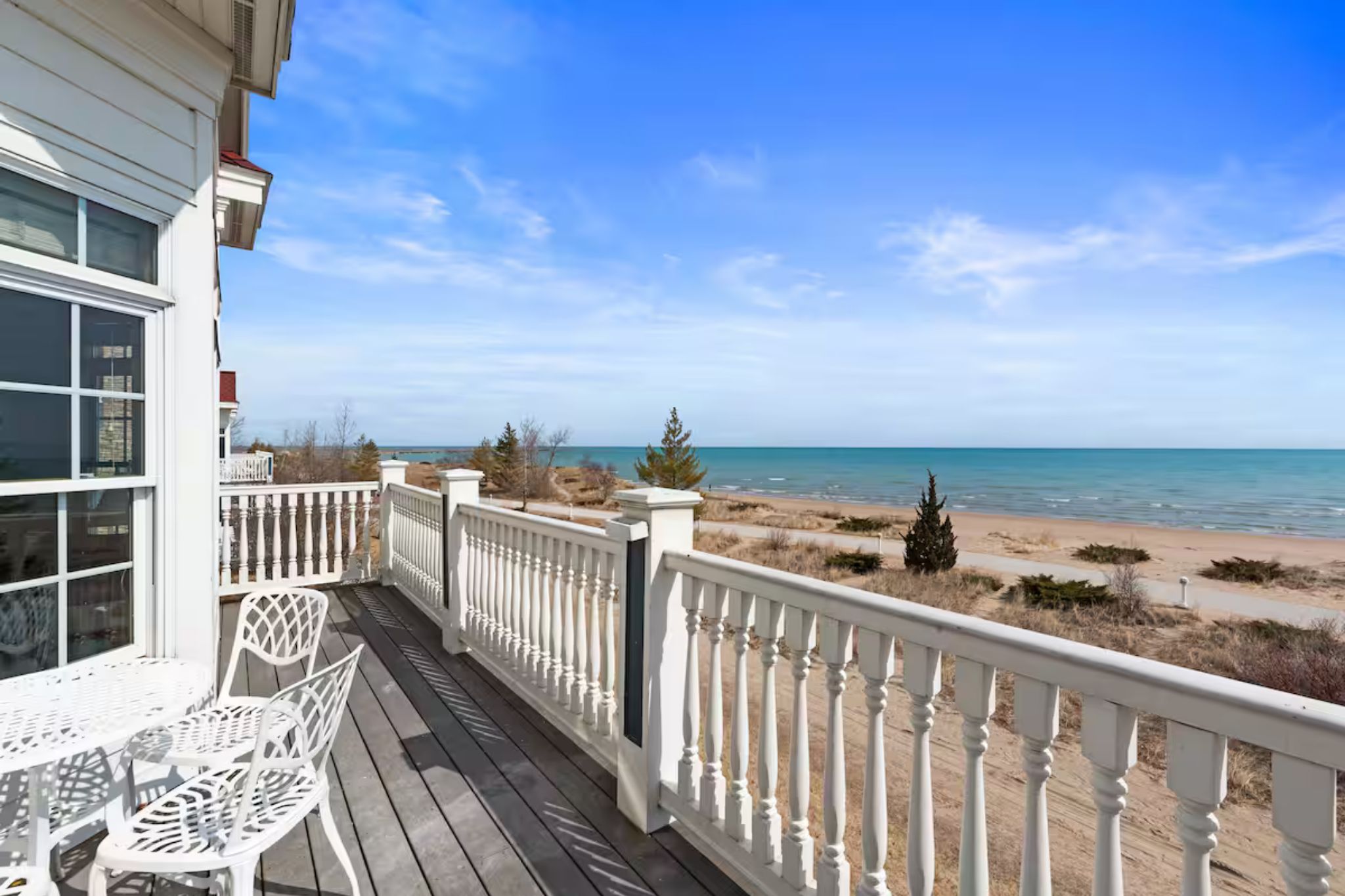 A wooden deck with white railings overlooking a beach.