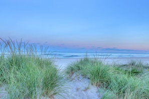 A beach with sand and grass in the foreground and a clear sky.