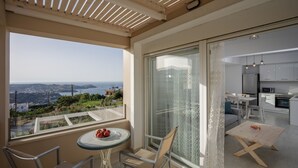 Ein Balkon mit Tisch und Stühlen, Blick auf das Meer und eine moderne Küche durch eine Glastür sichtbar.