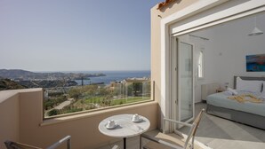 Ein Balkon mit Tisch und Stühlen, ein Bett mit einem Gemälde sowie Meer- und Landschaftsblick.