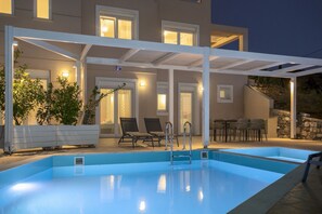 Piscina con pérgola blanca, mobiliario exterior y pared de piedra.