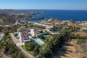 An aerial view of a coastal resort with multiple buildings, a swimming pool, and a view of the sea and hills. - Blue Hills Villas by Estia Orange 1 (Malevizi)