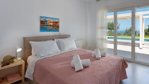 A hotel room with a bed, a nightstand, a painting, and a view of the sea. - Blue Hills Villas by Estia Orange 1 (Malevizi)