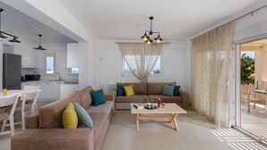 A modern living room with a sofa, coffee table, and a view of the kitchen and balcony. - Blue Hills Villas by Estia Orange 1 (Malevizi)