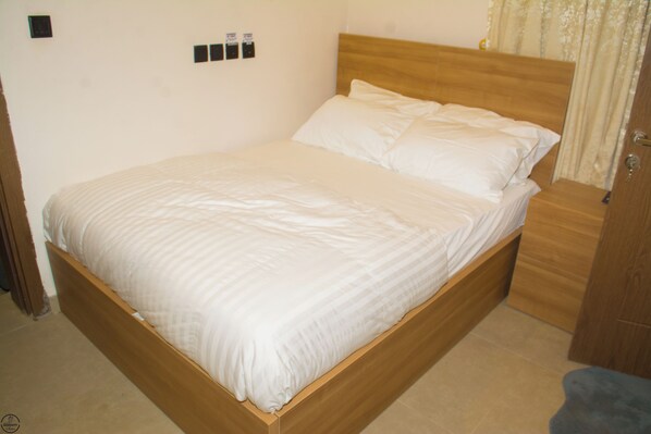 A neatly made bed with a wooden headboard and a matching nightstand. - 1BD Serenity Dubai Suites (Abuja)