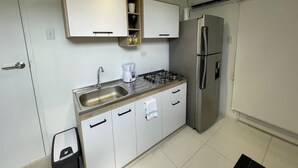 A compact kitchen with white cabinets, a stainless steel sink, a gas stove, a built-in oven, and a refrigerator.