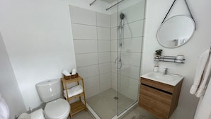 A modern bathroom with a glass-enclosed shower, a wooden vanity, and a toilet with a shelf.