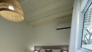 A bedroom with a bed, bedside lamps, a woven ceiling light, a window, and a patterned rug.