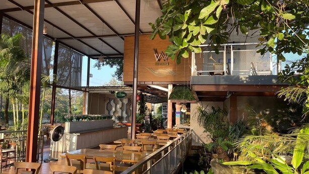 An indoor restaurant with wooden tables and chairs, a covered seating area, and a view of the outdoors. - TheRabbithome (Nakhon Nayok)