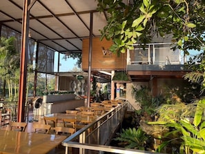 An indoor restaurant with wooden tables and chairs, a covered seating area, and a view of the outdoors.