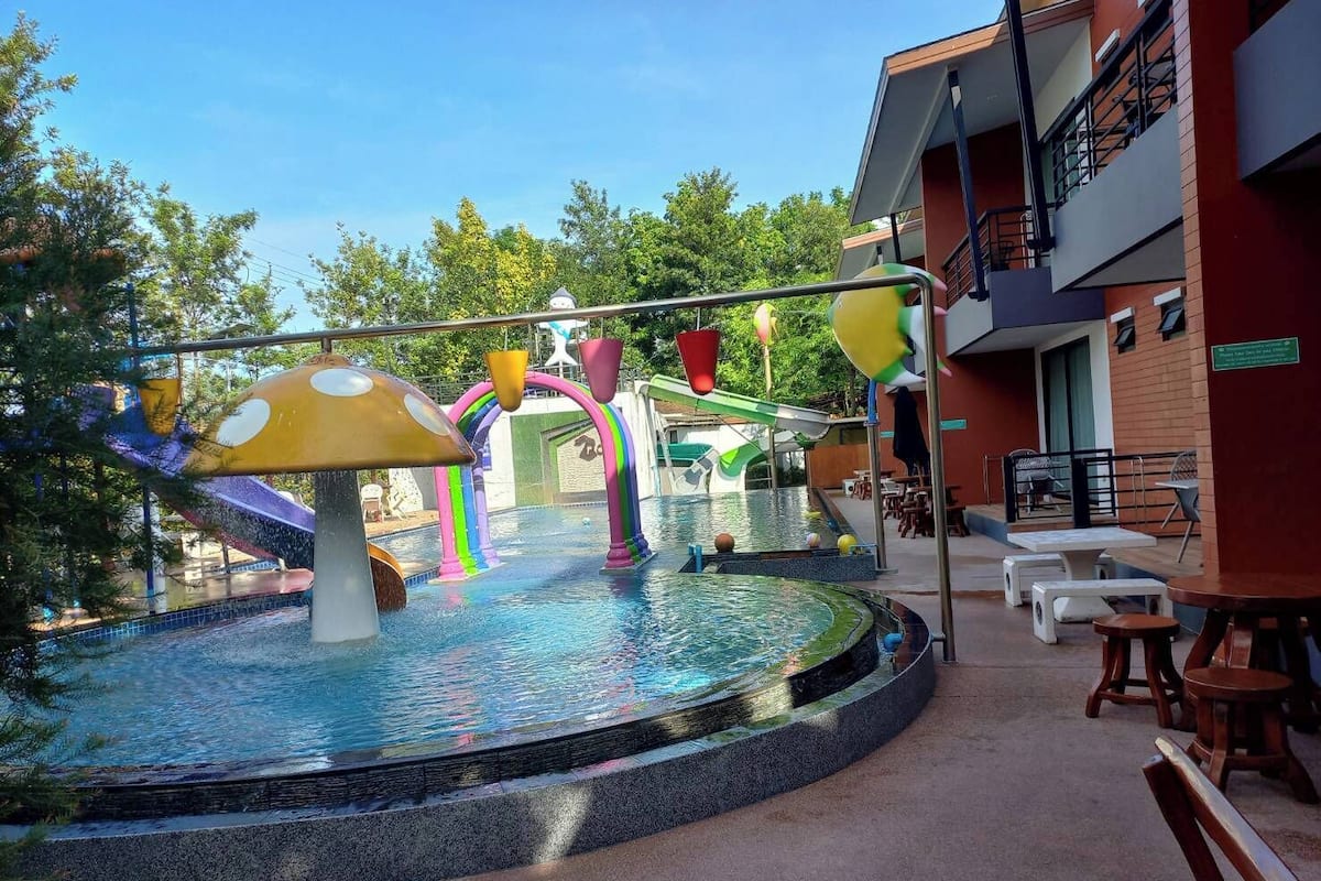 Uma área de piscina externa com escorregador, arcos coloridos e espaços para relaxar.