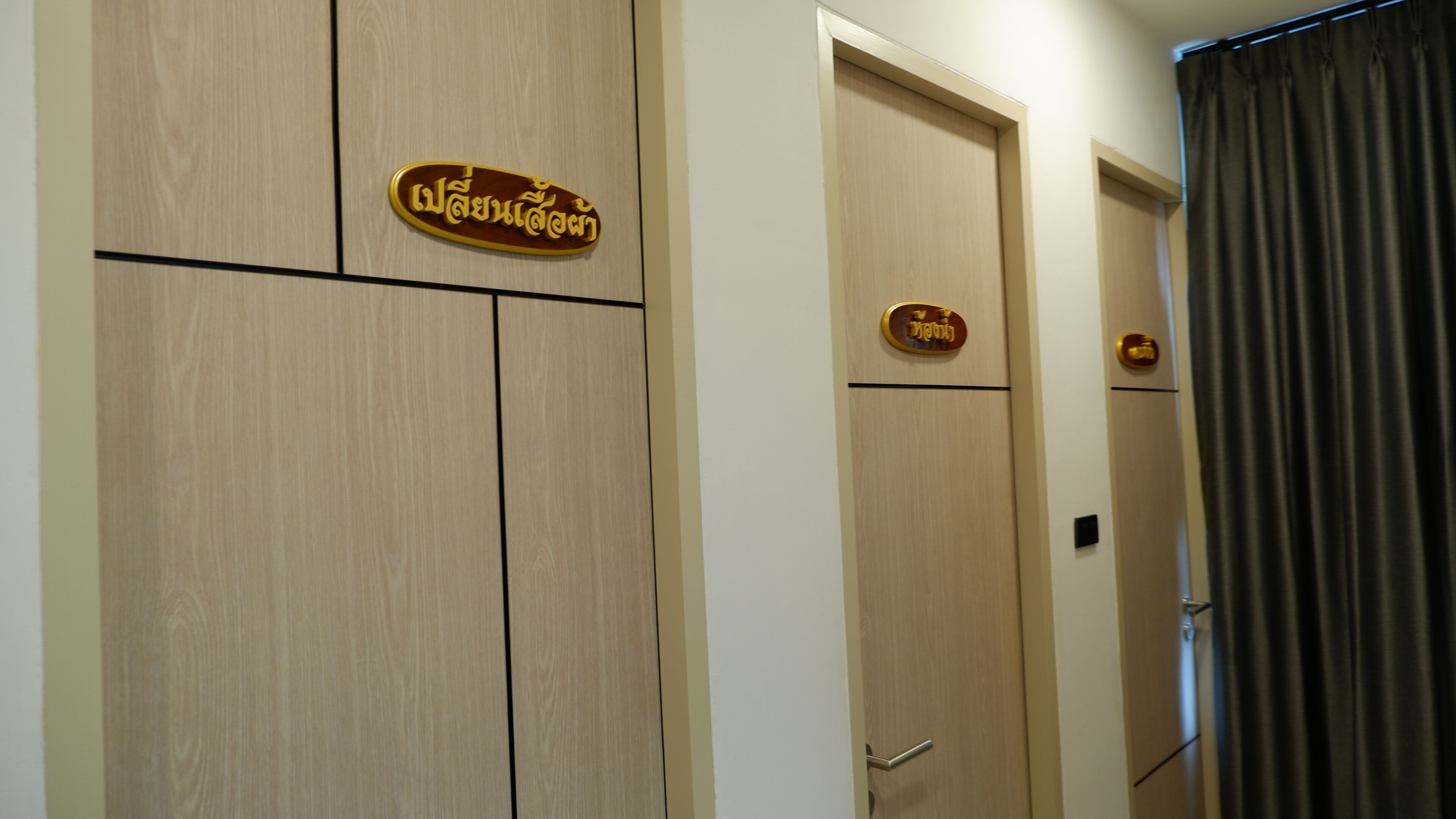 A hotel room with wooden doors, a sign with Thai script, and a curtain.