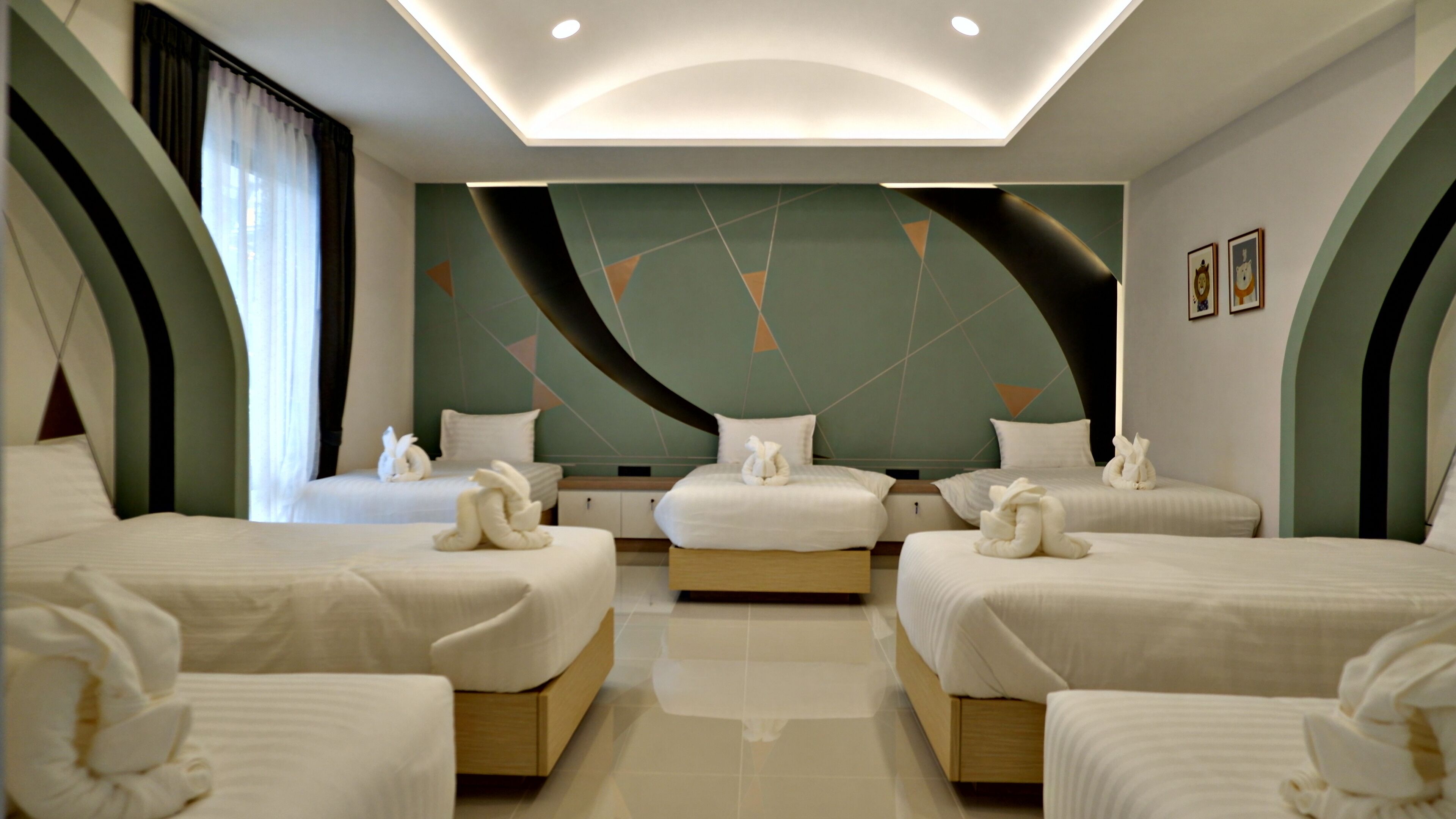 A hotel room with three beds, each with a white comforter and a towel. The room has a modern design with geometric wall patterns and recessed ceiling lighting.