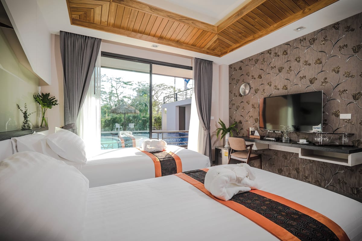 Quarto de hotel com duas camas, televisão, escrivaninha e vista para uma piscina.