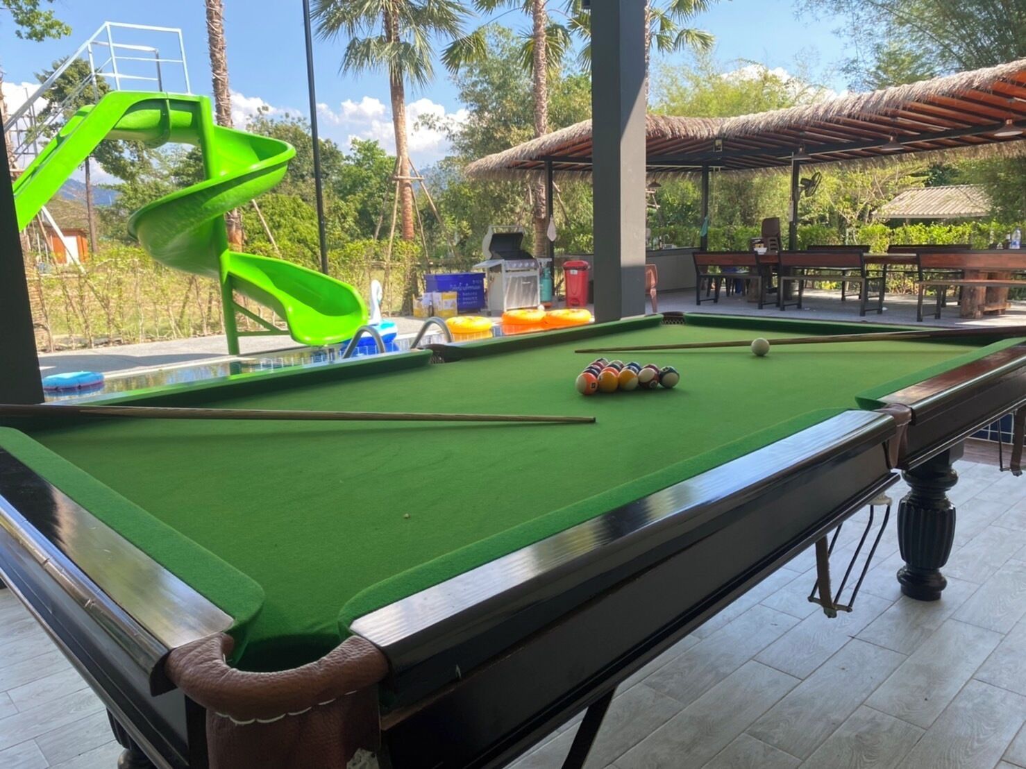 A pool table with a green felt surface, a pool cue, and billiard balls.