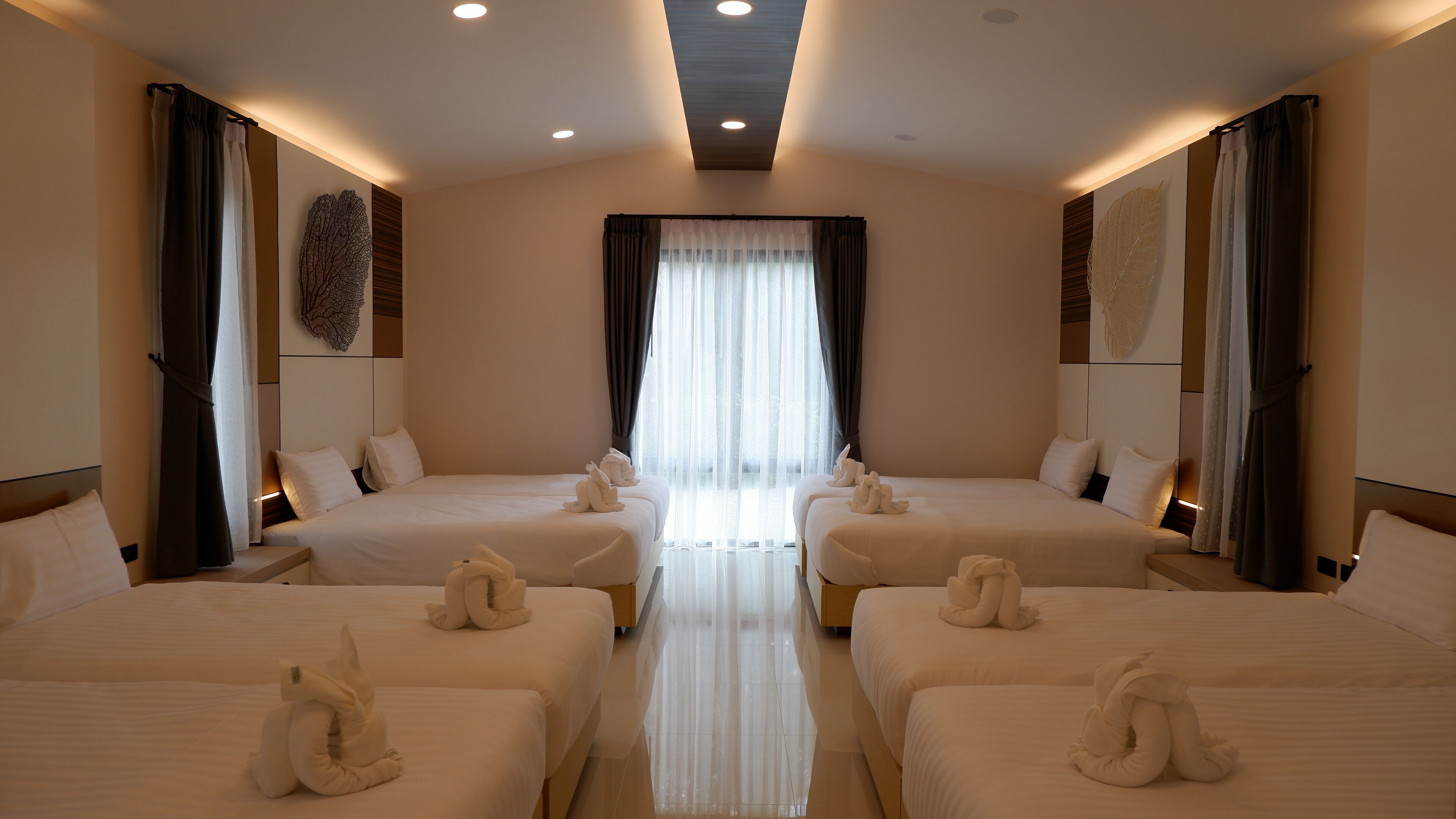 Habitación de hotel con dos camas, un ventanal con cortinas translúcidas e iluminación empotrada en el techo.