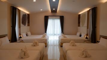 Habitación de hotel con dos camas, un ventanal con cortinas translúcidas e iluminación empotrada en el techo.