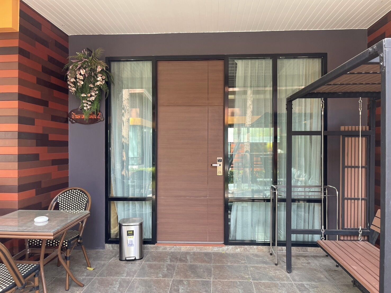 A modern outdoor seating area with a glass door, a trash bin, and a bench.