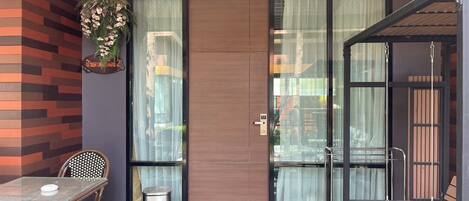 A modern outdoor seating area with a glass door, a trash bin, and a bench.