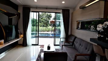 A modern living room with a large sliding glass door leading to a pool area, a flat-screen TV, a grey sofa, and a coffee table.