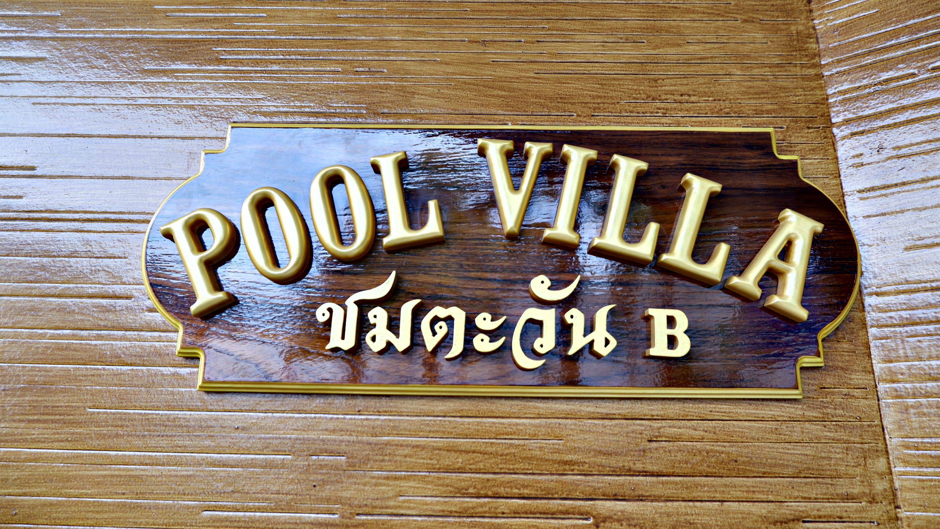 Une pancarte en bois portant l’inscription « POOL VILLA » et, en dessous, quelques caractères d’une langue autre que l’anglais.