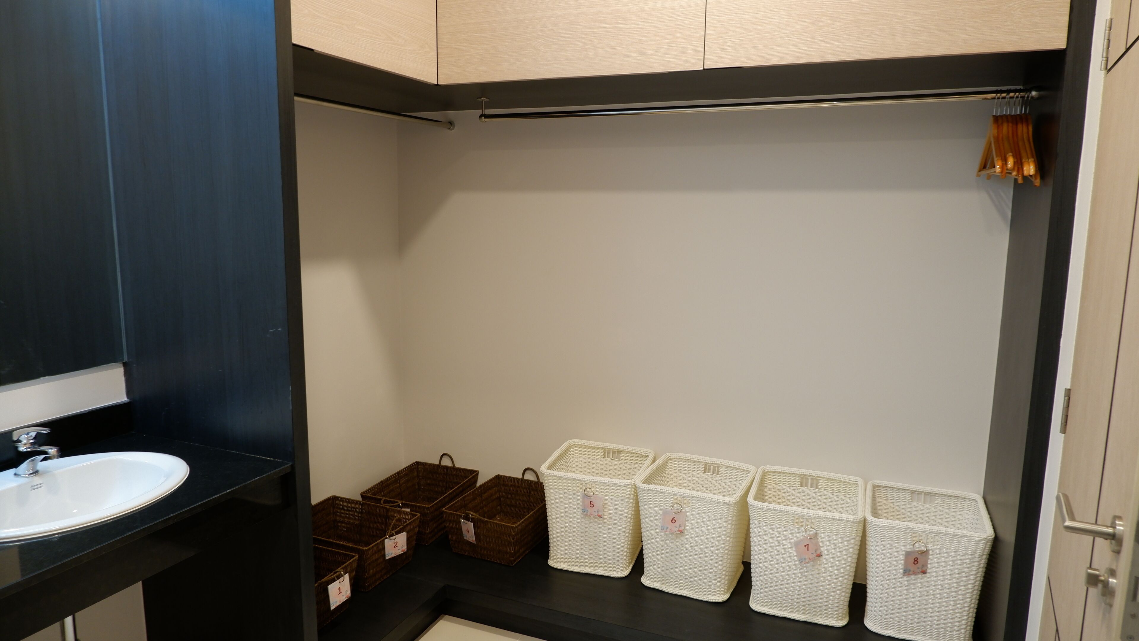 A bathroom with a black countertop, a white sink, and storage baskets labeled with numbers.