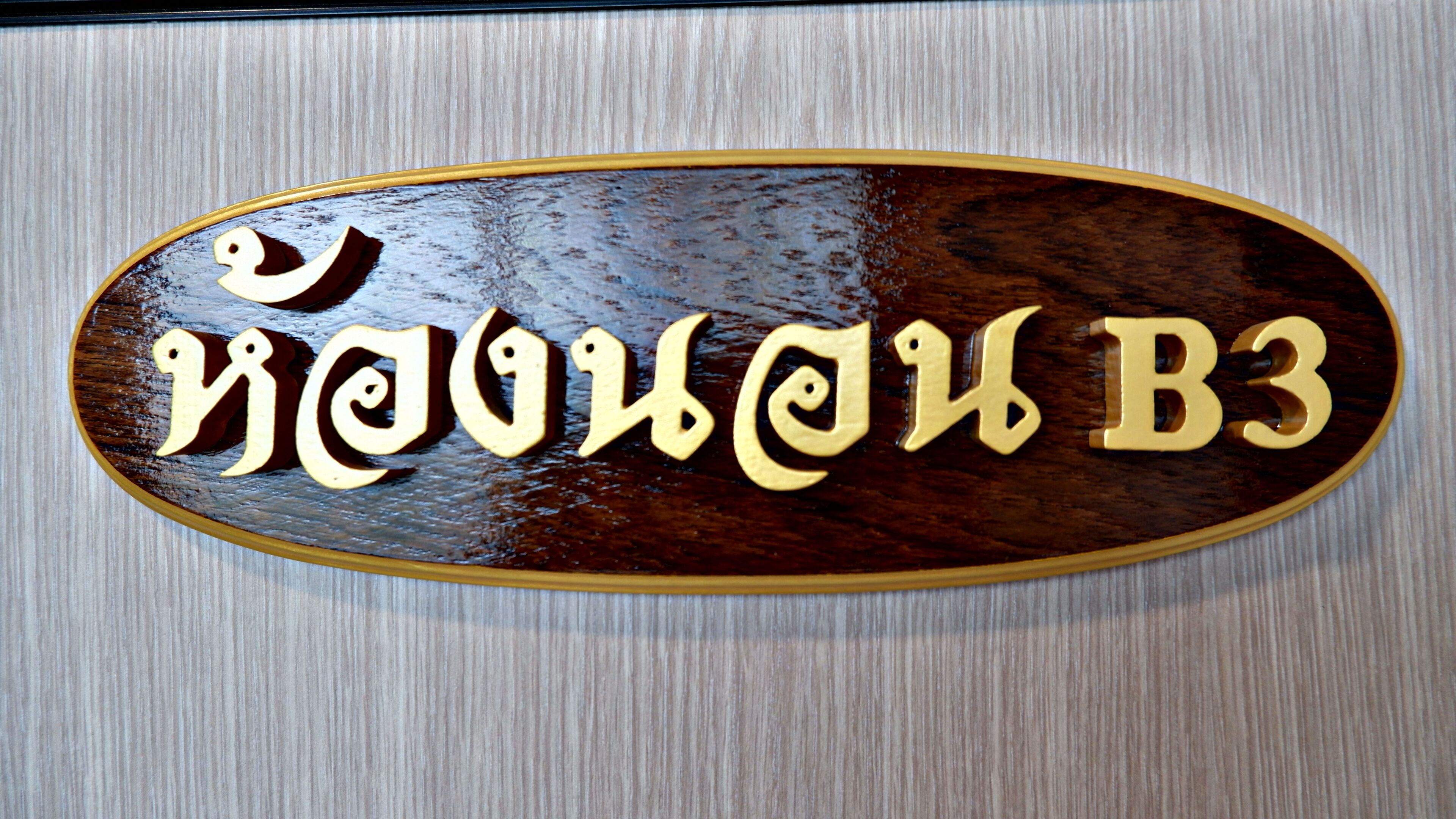 A wooden sign with carved text, likely indicating a room or location within a building.
