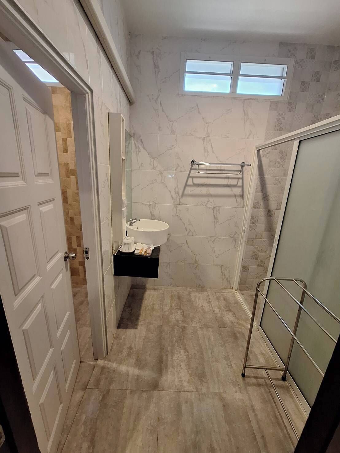 A bathroom with a marble wall, a sink, a towel rack, and a shower area.