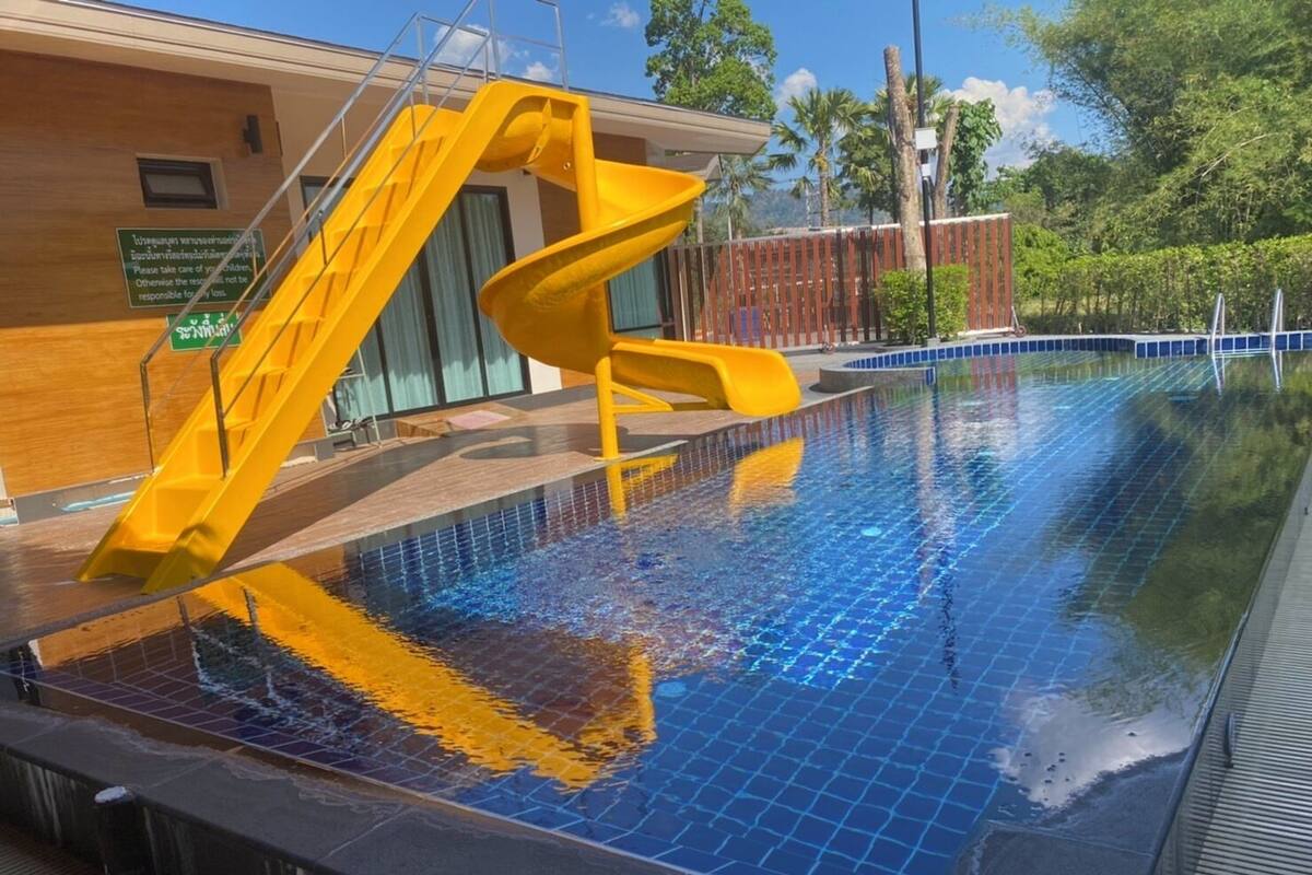 Piscina com um escorrega amarelo e um edifício de madeira ao fundo.