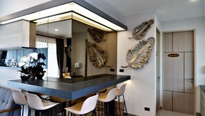 A modern kitchen with a central island, white chairs, and decorative golden leaves on the wall. - TheRabbithome (Nakhon Nayok)