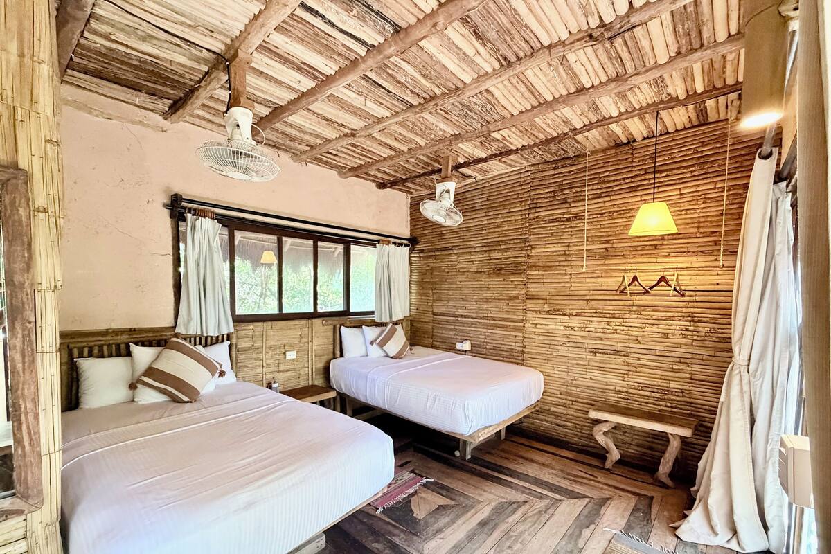 A rustic room with two beds, a wooden ceiling, and a window with curtains.