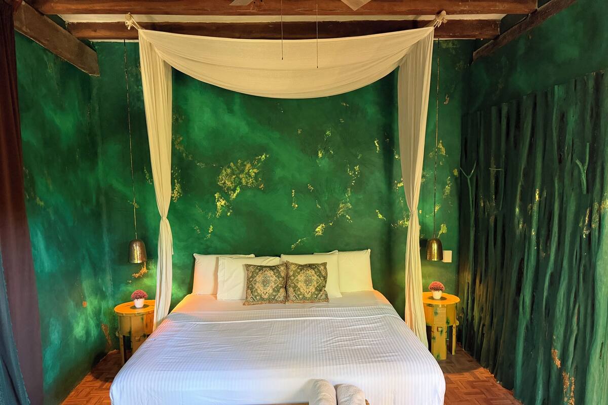 A bed with a canopy, a small table with a vase, and a wooden bench with towels.