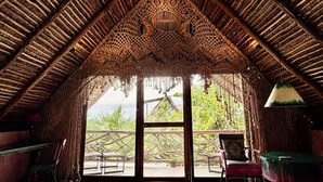 An interior with a thatched roof, a large window, and a view of greenery outside. - Alma Libre Hotel Tulum (Tulum)