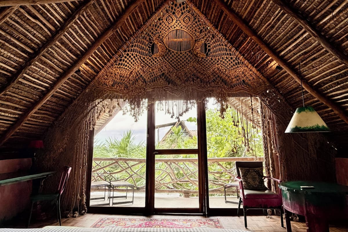 An interior with a thatched roof, a large window, and a view of greenery outside.