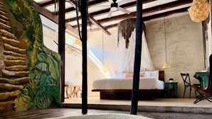 A room with a bed, a small table, a chair, a hanging light fixture, and a wall with a mural. - Alma Libre Hotel Tulum (Tulum)