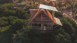 A thatched-roof house with a balcony, surrounded by dense tropical vegetation and a beach in the background. - Alma Libre Hotel Tulum (Tulum)