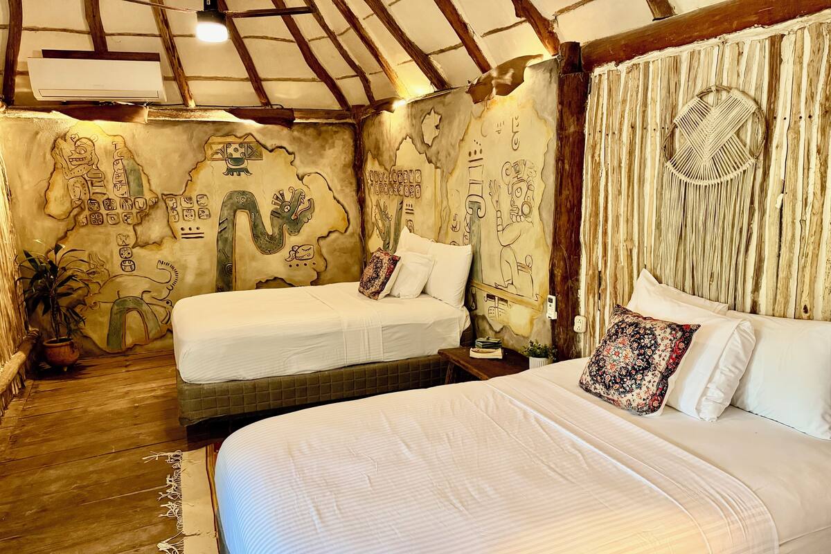 A room with two beds, a wooden floor, and a ceiling with exposed beams.