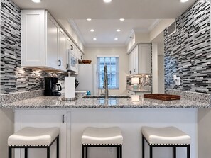 Una cocina moderna con armarios blancos, encimera de mármol y una isla integrada con taburetes de bar.
