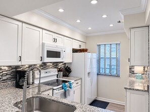 Una cocina moderna con gabinetes blancos, un lavamanos de acero inoxidable, un microondas y una estufa.