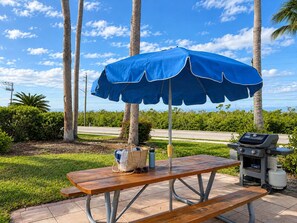 Montaje de picnic al aire libre con una mesa, una parrilla y una sombrilla azul.