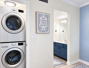 A laundry area with stacked washers and dryers, a wall-mounted light switch, and a framed inspirational quote. - 2BR Sandpiper Key – Bright, Stylish & Coastal (Englewood)