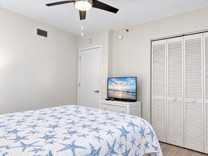 Une chambre à coucher avec un lit, un téléviseur posé sur un meuble, un ventilateur de plafond, une porte et un placard.