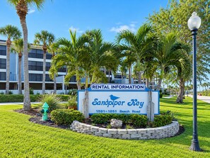 Un panneau d’information sur les locations à Sandpiper Key, situé au 1591-1651 Beach Road, avec en arrière-plan des palmiers et un bâtiment.