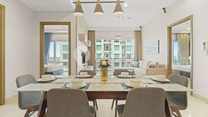 Een eetruimte met een lange tafel gedekt voor vier personen, een bloevas en uitzicht op een balkon met een gebouw op de achtergrond.