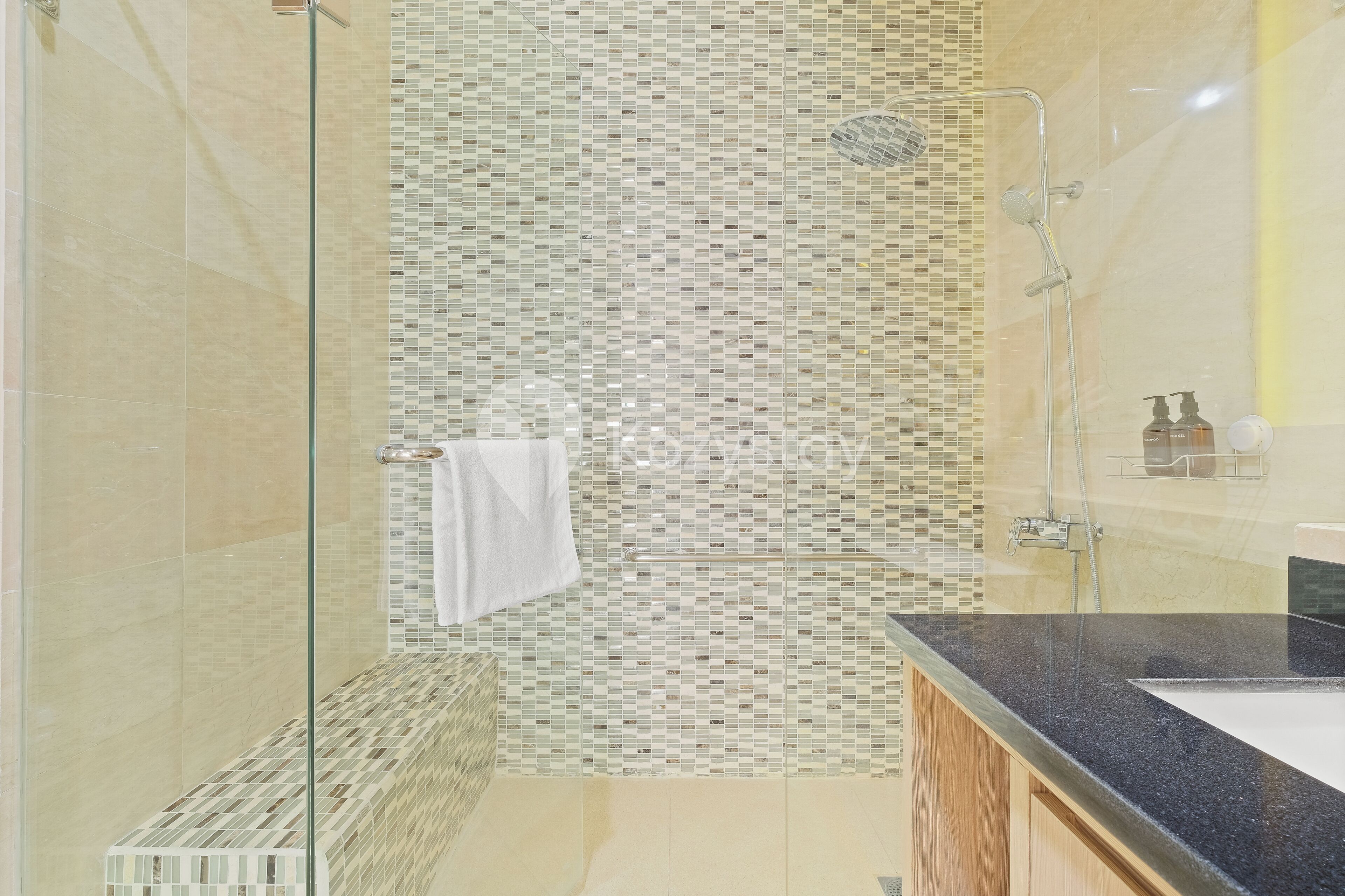 Une salle de bain moderne dotée d’une douche à paroi de verre, d’un mur de mosaïque et d’un lavabo sur plan de toilette noir.